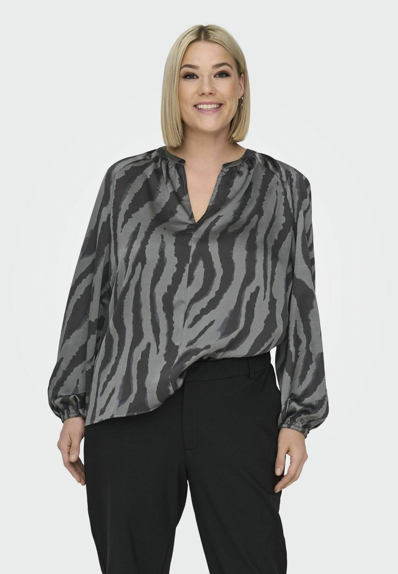 Grå och svart blus med tigerstrimmigt mönster, V-ringning och långa ärmar; matchad med svarta byxor. Mjuk, sidenliknande textur.