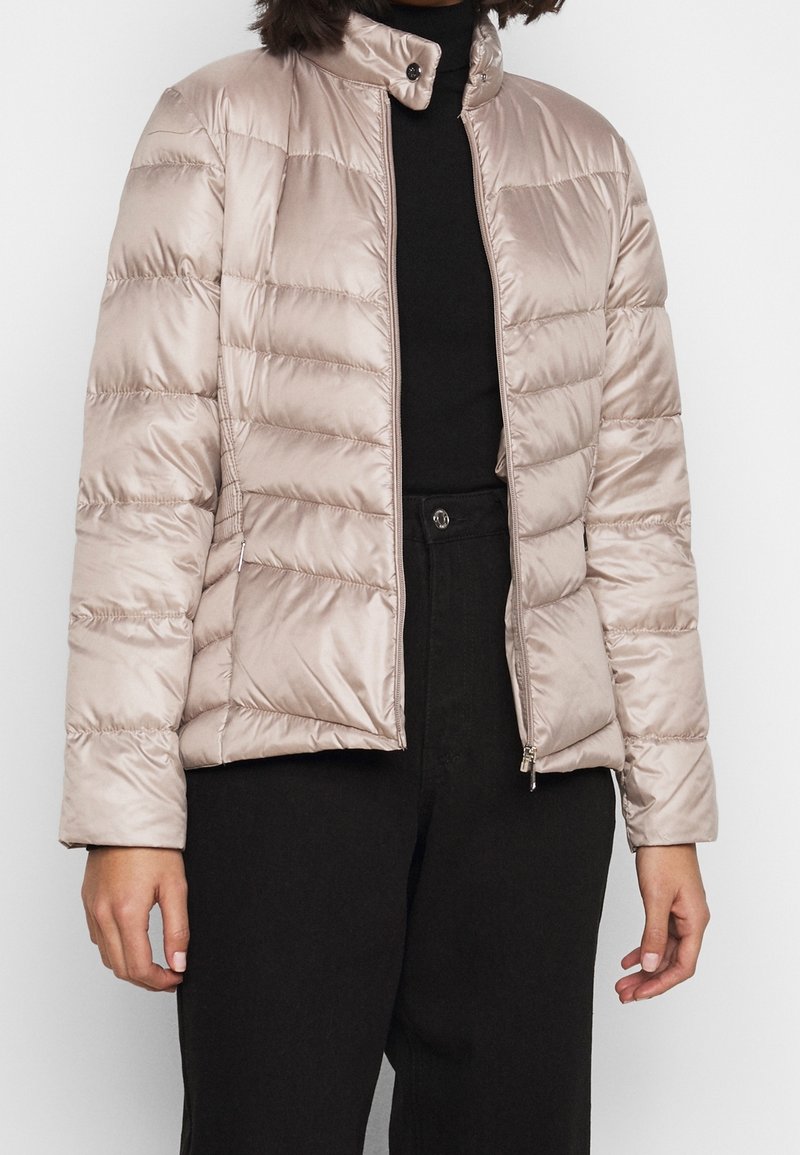 Pružná bunda z lesklého béžového saténového materiálu, vybavená vysokým límcem, zipovým zapínáním a vodorovným prošívaným vzorem. Měkká textura.