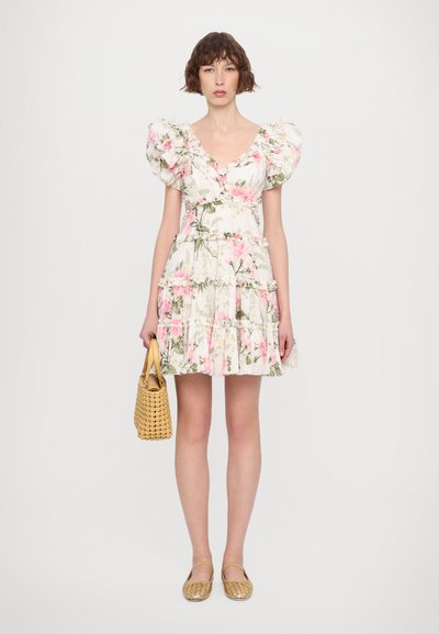 Witte bloemenjurk met roze rozen, gerimpelde pofmouwen, gelaagde rok, gecombineerd met een geweven gele tas en gouden platte schoenen.