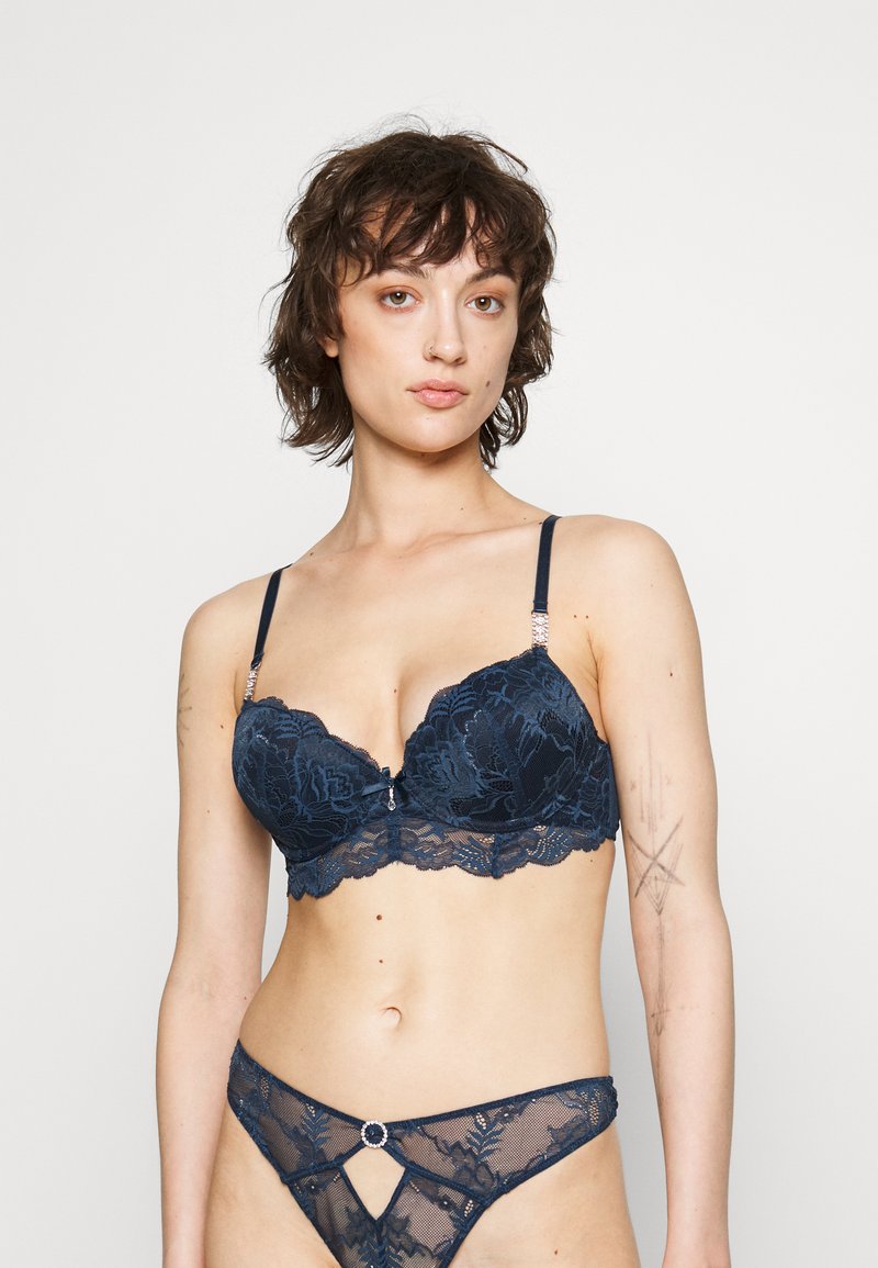 Navy blauwe kanten bh en string set met bloemenpatronen. De bh heeft onderbedrading, verstelbare schouderbanden en een decoratieve accent in het midden.