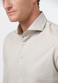 Lichtbeige shirt met een zachte textuur, voorzien van een staande kraag en drie knopen aan de voorkant. Tailored ontwerp, zonder zichtbare patronen.