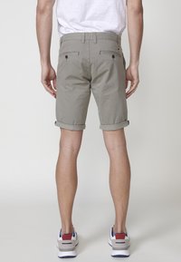 Pantaloni scurți gri deschis din bumbac, cu tiv rulat, două buzunare spate cu nasturi și fermoar. Purtați cu adidași albi.