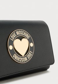Borsa a tracolla nera in ecopelle con logo circolare dorato che presenta una forma a cuore e il testo "LOVE MOSCHINO" con dettagli sul davanti.