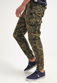 Kamouflagemönstrade cargobyxor i grönt och brunt, med tapered passform, elastiska muddar, flera fickor och en lätt tygkvalitet.