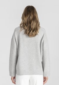 Szary sweter wykonany na drutach o luźnym kroju, z prążkowanymi mankietami i dołem, charakteryzujący się miękką fakturą i obniżonymi ramionami, widziany z tyłu.