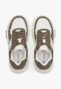 Białe i brązowe sneakersy mają perforowany przód, okrągłe sznurówki i detale logo. Gruba podeszwa ma kremowy kolor i gładką teksturę.