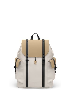 Beige og cremefarvet rygsæk med sorte stropper, klaplukning, to sidelommer og topgreb, vist mod en hvid baggrund.