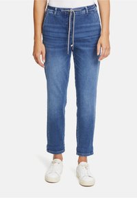 Pantalones de mezclilla azul claro con cintura con cordón, ajuste estrecho y puños enrollados. Combinados con zapatillas blancas para un look informal.