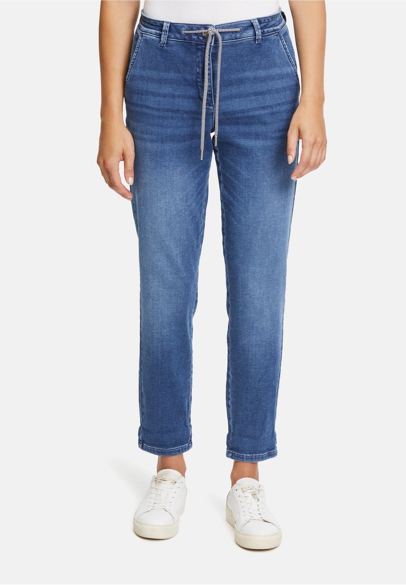 Pantalones de mezclilla azul claro con cintura con cordón, ajuste estrecho y puños enrollados. Combinados con zapatillas blancas para un look informal.