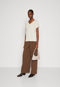 T-shirt avorio con scollo a V e maniche corte abbinato a pantaloni larghi marroni. Gli accessori includono una borsa a spalla beige e stivali con tacco quadrato marroni.