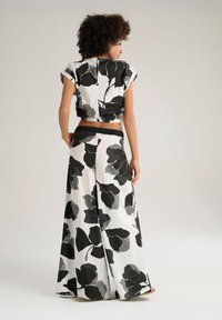 Top floreale in bianco e nero, con maniche arrotolate, accorciato e abbinato a pantaloni larghi in bianco e nero con motivo; vita elasticizzata, tessuto morbido.