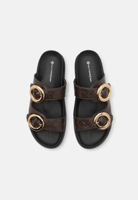 Brown vegan slide sandals with two wide, quilted straps featuring gold circular buckles, and a textured black sole for grip.