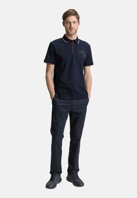 Marineblå polo T-shirt med røde detaljer, kortærmede, og knapkrave, parret med mørke bukser og sorte sneakers.
