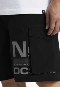 Čierne cargo šortky z texturovanej látky, s veľkou bočnou kapsou a potištenými grafickými prvkami v sivej farbe, navrhnuté na športové použitie.