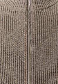 Suéter de punto acanalado color caqui con cuello alto y cremallera de longitud completa. Presenta un patrón texturizado y cierre con cremallera metálica lisa.