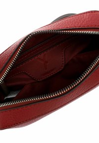 Borsa a mano in pelle rossa con superficie texturizzata, chiusura con cerniera e interno foderato in tessuto che presenta un piccolo scomparto e un logo impresso.