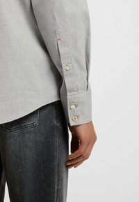 Helles graues Hemd mit einem strukturierten Muster, ausgestattet mit einem geknöpften Manschette und kontrastierenden orangefarbenen Akzenten. Kombiniert mit einer dunklen Jeans.