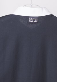 Námořnický polo tričko s bílým límečkem, s etiketou Red Bull Racing x Pepe Jeans. Hladká textura, čisté linie a minimalistický design.