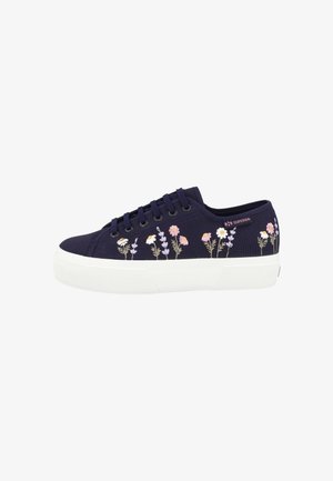 Zapatilla deportiva baja azul marino con suela gruesa blanca y flores bordadas en rosa, blanco y morado a lo largo del lateral, con cordones negros.