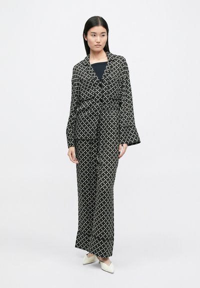 Μαύρο και άσπρο κα patterned δύο κομμάτι σύνολο που περιλαμβάνει ένα χαλαρό, μακρυμάνικο τζάκετ και παντελόνια με φαρδιά πόδια, φτιαγμένο από ανάλαφρο ύφασμα.