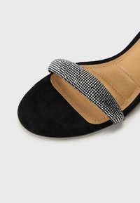Must must sandaalid laia musta rihmaga, millel on metallilised, sädelevad emailid. Sile pruun sisetald ja ümar varvaste kuju.
