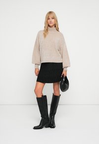 Pulover bej pufoș cu mâneci bulă, fustă neagră cu dungi verticale, cizme negre până la genunchi și un geantă neagră.