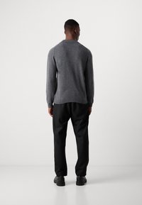 Gray knitted sweater with a relaxed fit, featuring long sleeves and a slightly curved hem, paired with black loose-fitting trousers.