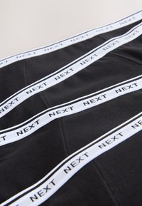 Tissu noir avec texte et rayures blanches "NEXT". Texture plate avec des accents cousus et un motif géométrique créé par les lignes.