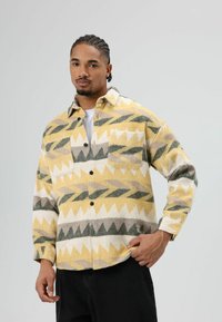 Flanellen overhemd in geel, wit, groen en bruin met een zigzagpatroon. Voorzien van twee voorzakken, knoopsluiting aan de voorkant en een ontspannen pasvorm.