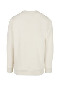 Kremo spalvos džemperis su apvalia iškirpte, ilgomis rankovėmis ir ribotais rankogaliais. Lygus paviršius ir minimalistinis dizainas be matomų raštų.