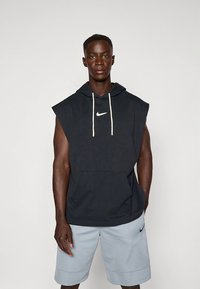 Hoodie azul-marinho sem mangas com bolso frontal e cordões brancos; apresenta um pequeno logótipo Nike branco no peito. Combinado com calções cinza claro.