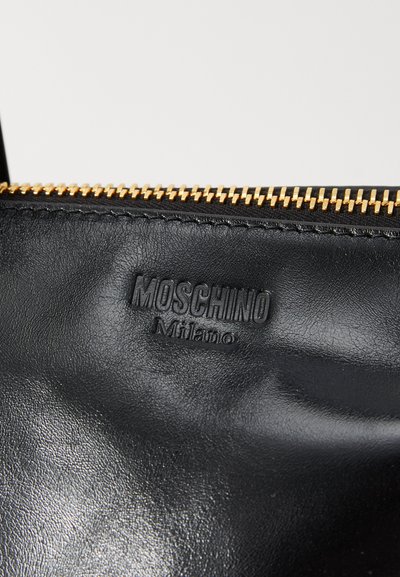 Čierna kožená taška s textúrovaným povrchom, so zlatým zipsom a embosovaným logom "Moschino Milano". Aklóz pohľad na hornú časť.