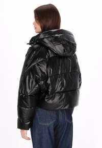 Fekete steppelt dzseki fényes, texturált felülettel, túlméretezett kapucnival és rövid fazonnal, varrott panelekkel és patentos záródásokkal.