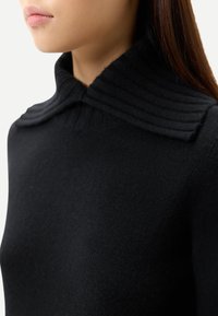 Svart ribbstickad tröja med hög, strukturerad krage och slät textur, med en smal passform.