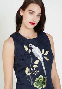 Vestido sin mangas de color azul marino con un patrón texturizado, que presenta bordados en blanco de aves y flores en amarillo y verde.