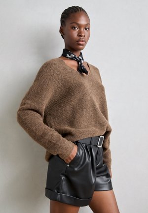 Brown oversized sweater in textured knit, paired with black leather shorts featuring a wide waistband and silver buckle detail.