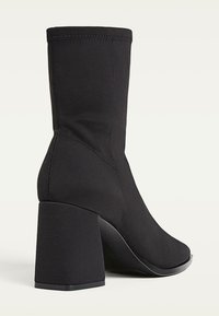 Stivale nero alla caviglia realizzato in tessuto elasticizzato, con punta quadrata e tacco chunky, caratterizzato da una texture liscia e dettagli di cucitura minimali.