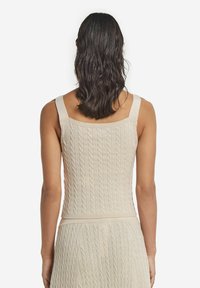 Top in maglia beige con spalline larghe, caratterizzato da un motivo a treccia testurizzato e una silhouette aderente. Rifinito con un orlo dritto.