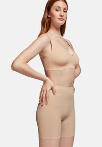 Nude seamless bra and high-waisted shorts made of stretchy fabric, featuring thin straps and a smooth, matte texture.