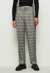 Grå rutiga byxor med skräddarsydd passform, två framknappar och sidofickor. Tillverkade av ett texturerat tyg med ett klassiskt rutmönster.