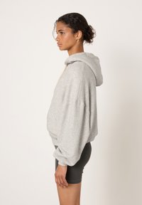 Siva jopa z rahlo prileganostjo, z ruto s trakcem za povlek in mehko teksturo. Kombinirana s črnimi kolesarskimi hlačami, ki poudarjajo sproščen slog.
