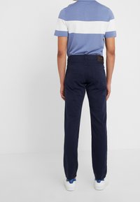 Pánské námořnické kalhoty z bavlny s rovnýcm střihem, které mají design zadní kapsy a značkovou nálepku na pásku. Kombinují se s modro-bílou pruhovanou košilí.