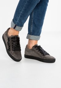 Le sneaker grigie in suede presentano lacci neri satinati e una suola in gomma nera testurizzata, arricchite da dettagli decorativi sui lati.