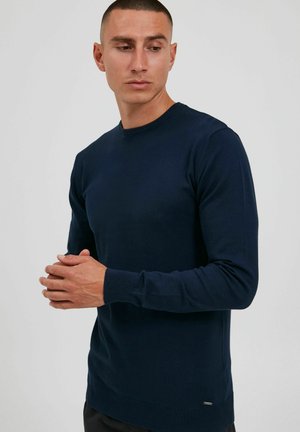 Navyblauer Pullover aus Strickmaterial mit rundem Halsausschnitt und gerippten Bündchen, ausgestattet mit einem kleinen Akzentlogo am Saum.