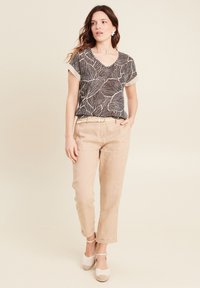 Zwart-wit top met een bladerenpatroon en een V-hals, gecombineerd met lichtbeige linnen broek en een gevlochten riem. De schoenen zijn witte espadrilles.