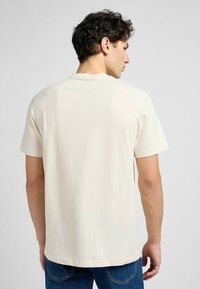 Kremowa bawełniana koszulka z krótkim rękawem i okrągłym dekoltem. Tył ma gładką strukturę i luźny krój.