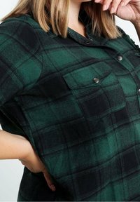 Zielono-czarna koszula w kratę wykonana z flaneli, z zapięciem na guziki, dwoma kieszeniami na piersi oraz krótkimi rękawami. Teksturowana tkanina.