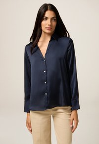 Navy Satin-Hemd mit langen Ärmeln, Kragen und geradem Saum. Mit perlenartigen Knöpfen auf der Vorderseite. Weiche, glatte Textur.