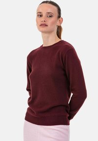 Pull en tricot bordeaux avec un col rond et des manches longues. Texture douce, poignets et ourlet côtelés. Associé à un bas rose clair.