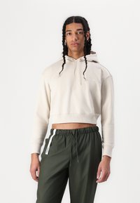 Cropped beige hoodie in soft fabric with a drawstring hood, featuring ribbed cuffs. Paired with dark green drawstring pants with side accents.